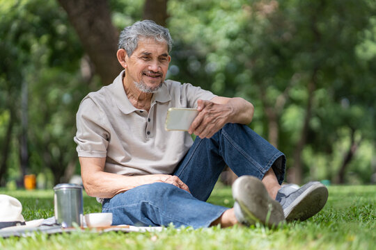 elderly pensioner man spend leisure time relaxing in urban park,sitting and surfing internet on smartphone