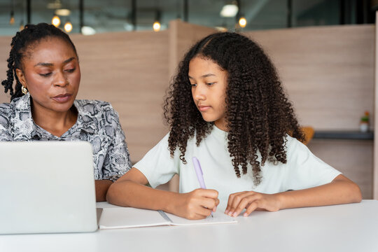 Mother helping daughter with homework using laptop at home, Woman tutor teaching young girl student writing notes on notebook, Teacher guiding kid girl learning online education on laptop