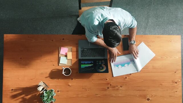 Top aerial view of manager working on laptop while looking at data analysis. Leader compare financial statistic graph while making decision at meeting table with document scatter around. Convocation.