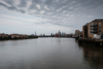 Naklejka premium River thames flowing past london skyline under overcast sky