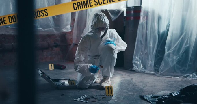 Crime scene specialist in protective clothing inspects trace evidence on the floor during a forensic investigation.