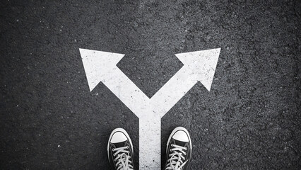 Fototapeta premium Person standing at a y-shaped path fork in the road choosing a direction with direction decision sneakers standing perspective crossroads motivation adventure opportunity strategy