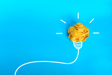 Crumpled yellow paper light bulb with white rays and large copy space on blue background  © kaliel