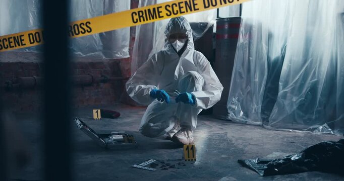 Forensic investigator in protective clothing examines and collects evidence at a secured crime scene marked with numbered evidence markers.