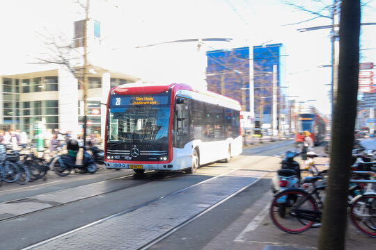 den haag, netherlands - march 18 2026: A bus moves on tracks in a busy city street. Many people are near bicycles and buildings in background