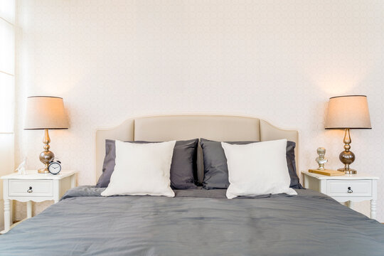 Cottage contemporary style bed headboard, light brown wallpaper wall with two table lamps beside the headboard, White pillow, Gray pillow and blanket