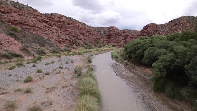 4K drone aerial view of La Poma, Salta, Argentina. Stunning Andean landscape with red rock mountains, green valleys and a river crossing the dramatic canyon scenery.