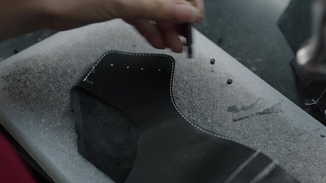 Worker hand-punches holes in leather shoe upper on workbench in factory setting