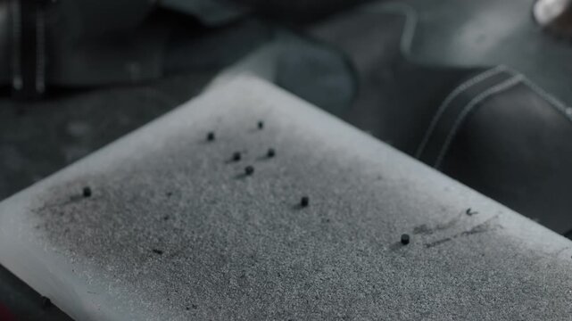Worker uses hand tools to punch holes in leather shoe part on workshop table