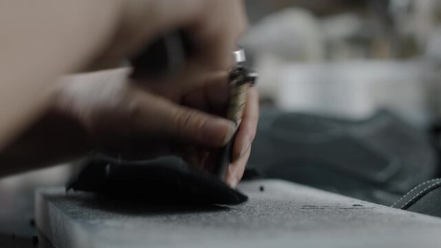 Worker handcrafting leather shoe parts with hand tool in workshop closeup