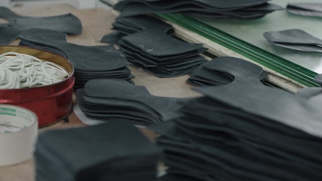 Stacks of cut leather pieces and tools on a workbench in a shoe production workshop
