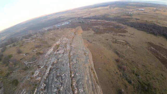Andean condors gliding just below the sheer cliff edge of Cerro Dorotea, overlooking a wide golden valley and distant hills near Puerto Natales, Chile, FPV aerial