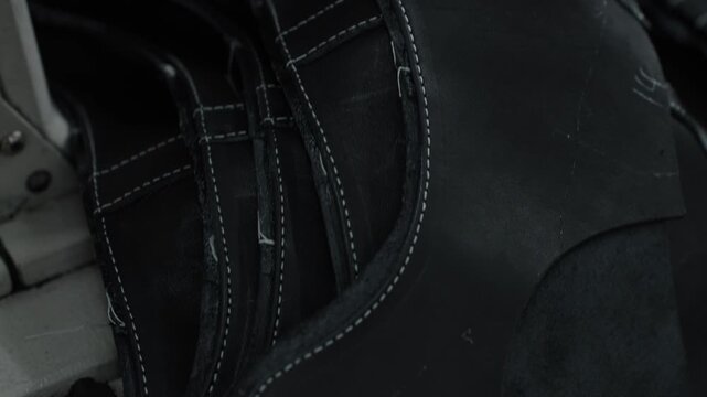 Stacked black leather shoe uppers with white stitching in a workshop setting