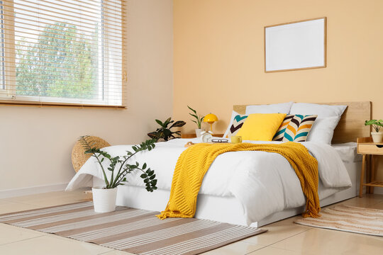 Modern bedroom interior with a comfortable bed, yellow blanket, decorative pillows, and Potted plants