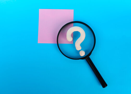 Magnifying glass framing a white question mark beside a pink note on blue background
