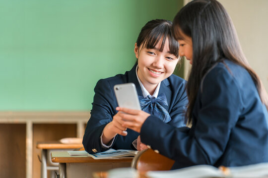 A middle school girl talking while looking at her smartphone in a school classroom.