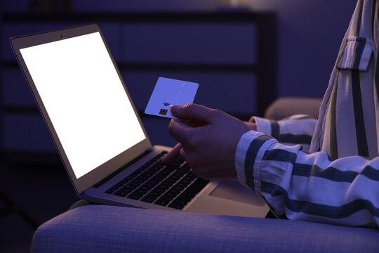 Young woman with credit card using laptop for online shopping on sofa in evening at home, closeup