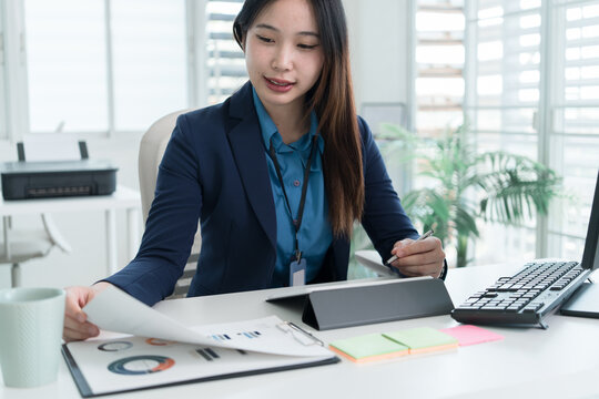 Young Businesswoman Working at Office Desk While Managing Documents and Mobile Communication.