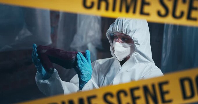 Forensic investigator examines physical evidence behind crime scene tape while processing a criminal investigation