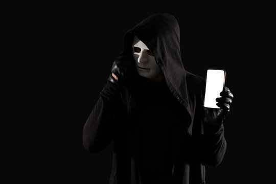 Male fraudster in mask with mobile phone on black background