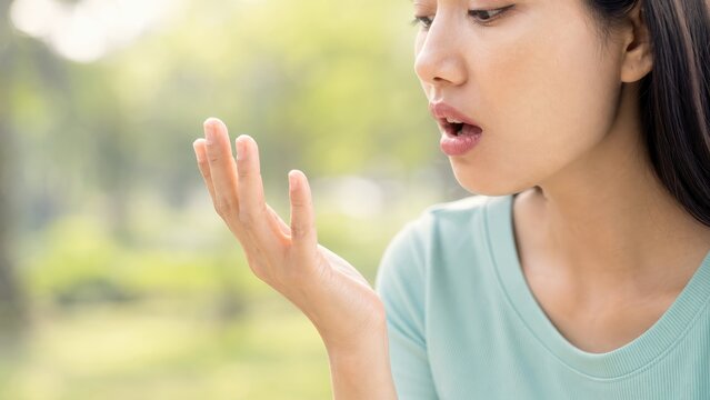 Young woman checking bad breath by smelling hand, oral hygiene and halitosis problem outdoors