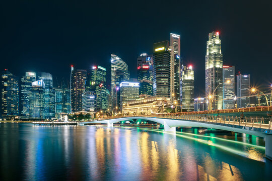 Illuminated Singapore financial district skyline viewed across Marina Bay at night, Jubilee Bridge ,colorful reflections, calm water, long exposure cityscape, iconic downtown