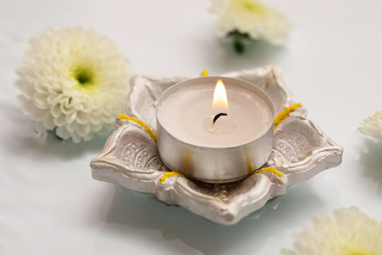 Diya lamp with burning candle and beautiful flowers in water on white background. Divaly celebration