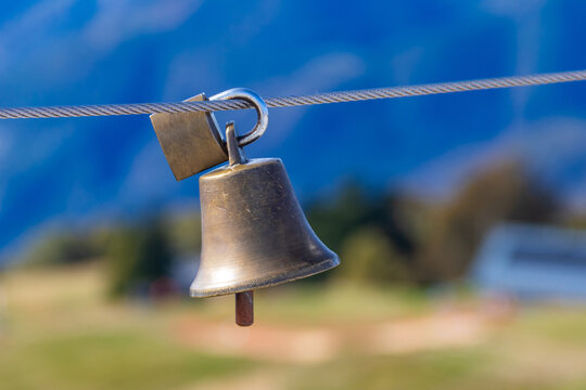 Traditional swiss bell hanging on a steel wire rope fencing with a blurred alpine mountain background