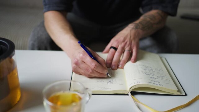 Person writing productivity book at desk, close-up view