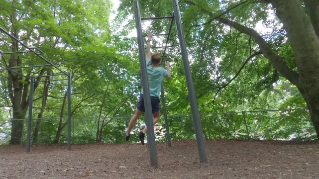 Young man hangs and does pull ups spinning around monkey bars at St. Hanshaugen calisthenics park in Oslo