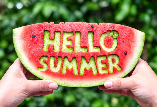 Hands holding a carved watermelon slice with hello summer text in outdoor setting