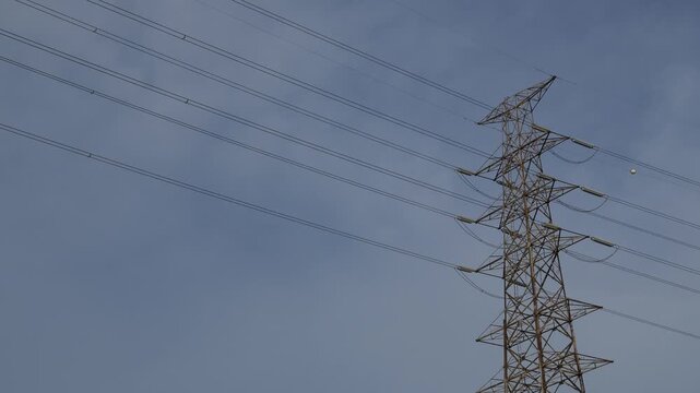Low angle view of tall steel electricity transmission tower pylon with high voltage power lines against clear blue sky