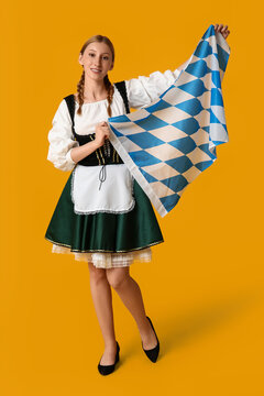 Beautiful happy Octoberfest waitress with Bavarian flag on yellow background