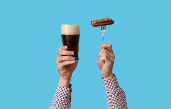 Hands with glass of beer and sausage on blue background