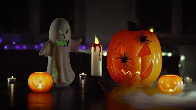 Pumpkin lantern sits on a dark wooden table surrounded by a glowing ghost figurine and flickering candles in a dim room decorated for a festive autumn holiday celebration with a mysterious atmosphere.