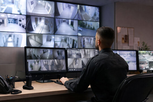 Security operator observing multiple CCTV camera feeds from corridors, entrances, and outdoor areas in a professional surveillance control room.