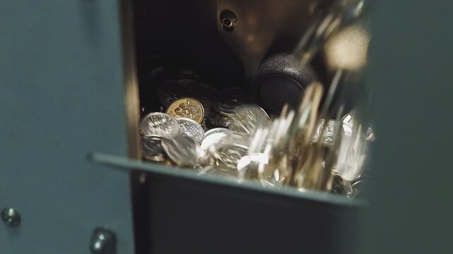 Coin collection falls into a dark metal box as financial savings are gathered together inside a secure storage container that represents the accumulation of wealth and long term monetary investments.