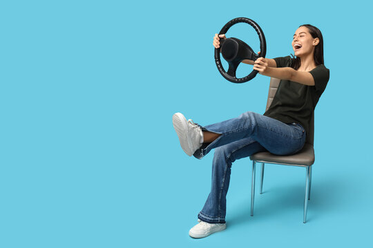 Happy young woman with steering wheel on blue background
