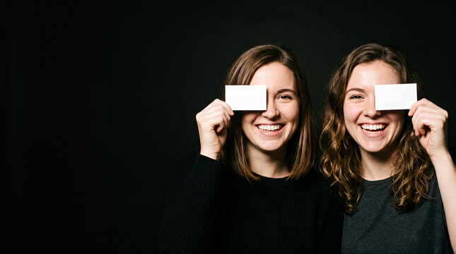 Two women holding white cards smiling against dark background