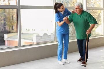 Fototapeta premium Nurse helping senior man with stick to walk at hospital