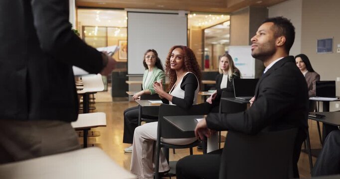 Speaker addresses audience in business seminar training. Professionals ask questions during a presentation in a classroom workshop. Corporate learning presentation workshop discussion concept.