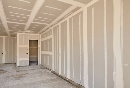 Interior of residential house under construction with freshly taped drywall panels on walls and ceiling, construction