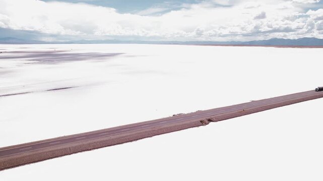 4K drone aerial view of a truck driving through Salinas Grandes in Jujuy, Argentina. Vehicles crossing the road surrounded by vast white salt flats and the dramatic Andean landscape.