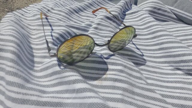 Sunglasses resting on striped towel with gradient colored lenses, long shadow cast from glasses