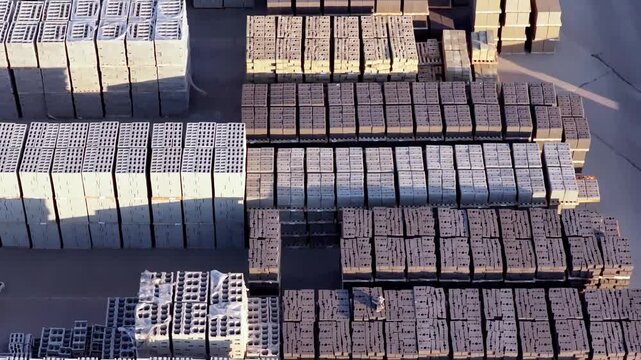 High angle drone video reveals rows of masonry block, segmental retaining walls, pavers, and fence block neatly organized in a sunrise-lit loading yard, casting long shadows.
