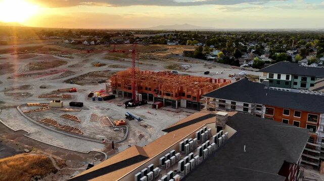 Wood-frame apartment construction project with tower crane earthworks and completed residential buildings in Taylorsville, Salt Lake County, Utah, United States, beneath Wasatch Range, drone parallax