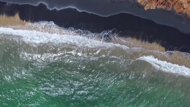 Top-down upward drone fly over emerald Caribbean waves washing onto dramatic Black Sand Beach on tropical environment, Vieques, Puerto Rico