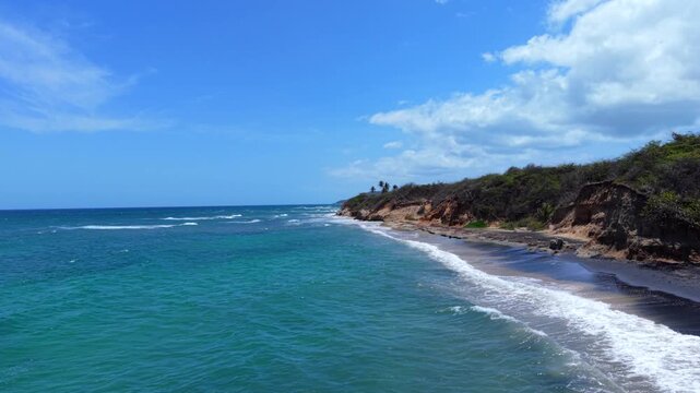 Low-altitude drone fly along Black Sand Beach endpoint view with distant beautiful tropical beach environment meeting rugged coastal cliffs, Vieques, Puerto Rico