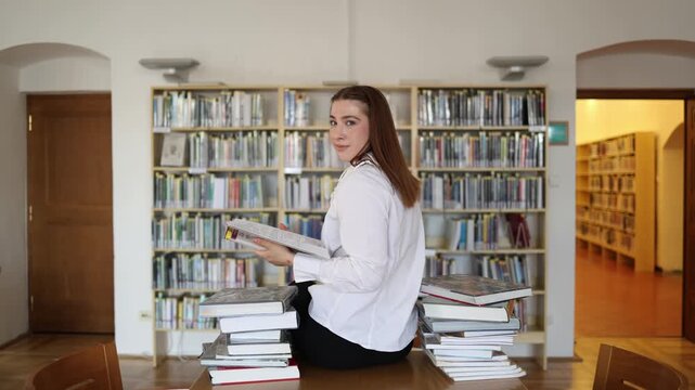 Confident young student selects textbooks for a productive study session in a university library smiling after organizing materials and planning her academic workload now