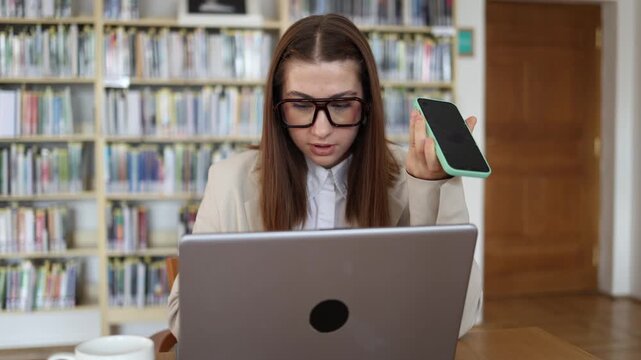 Business consultant speaks to an AI voice assistant on smartphone while using laptop in office testing how automation can speed up research planning and routine digital work